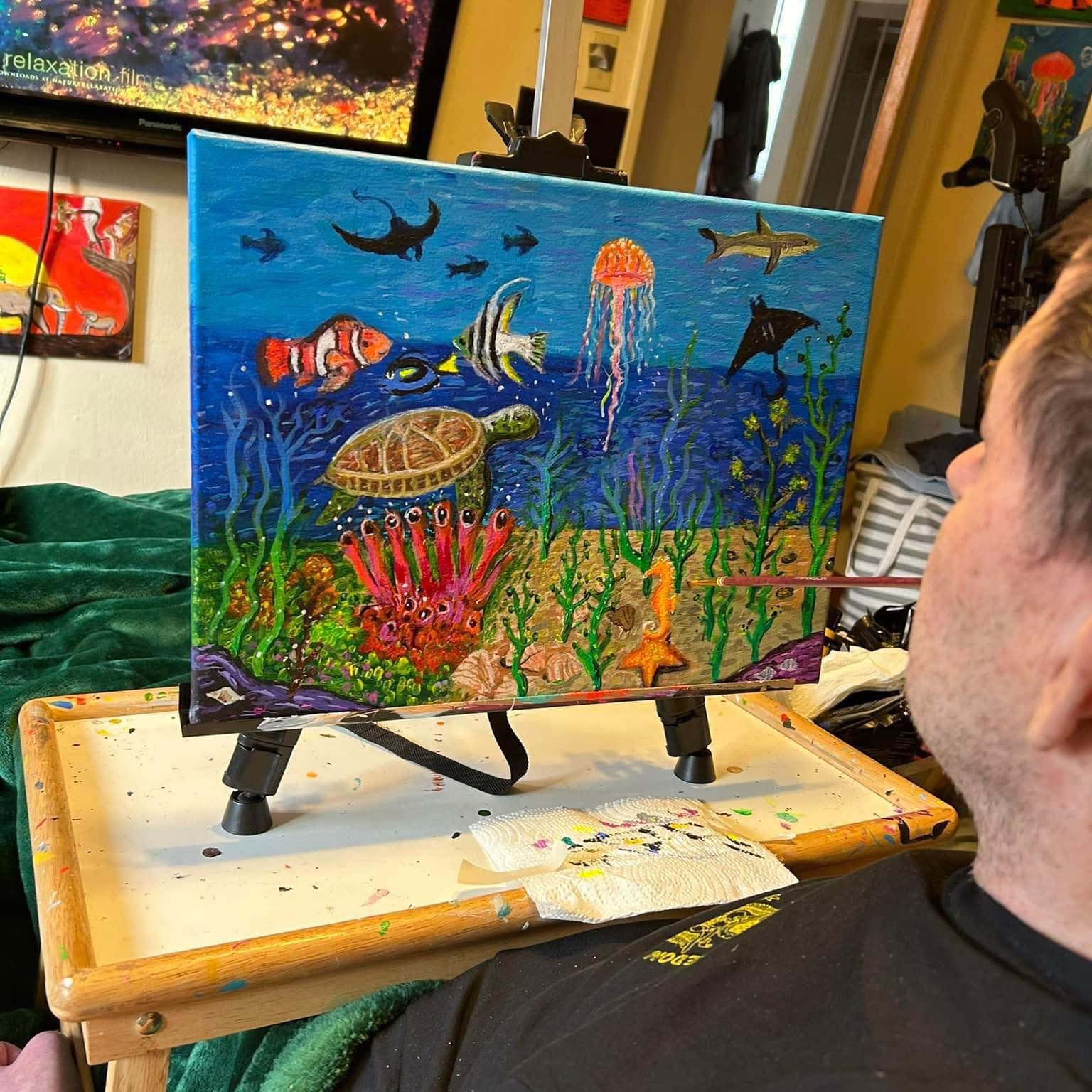 Paul O'Lone painting an underwater scene with a brush held in his mouth